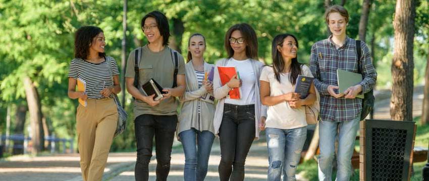 Students walking and talking carrying books outside 